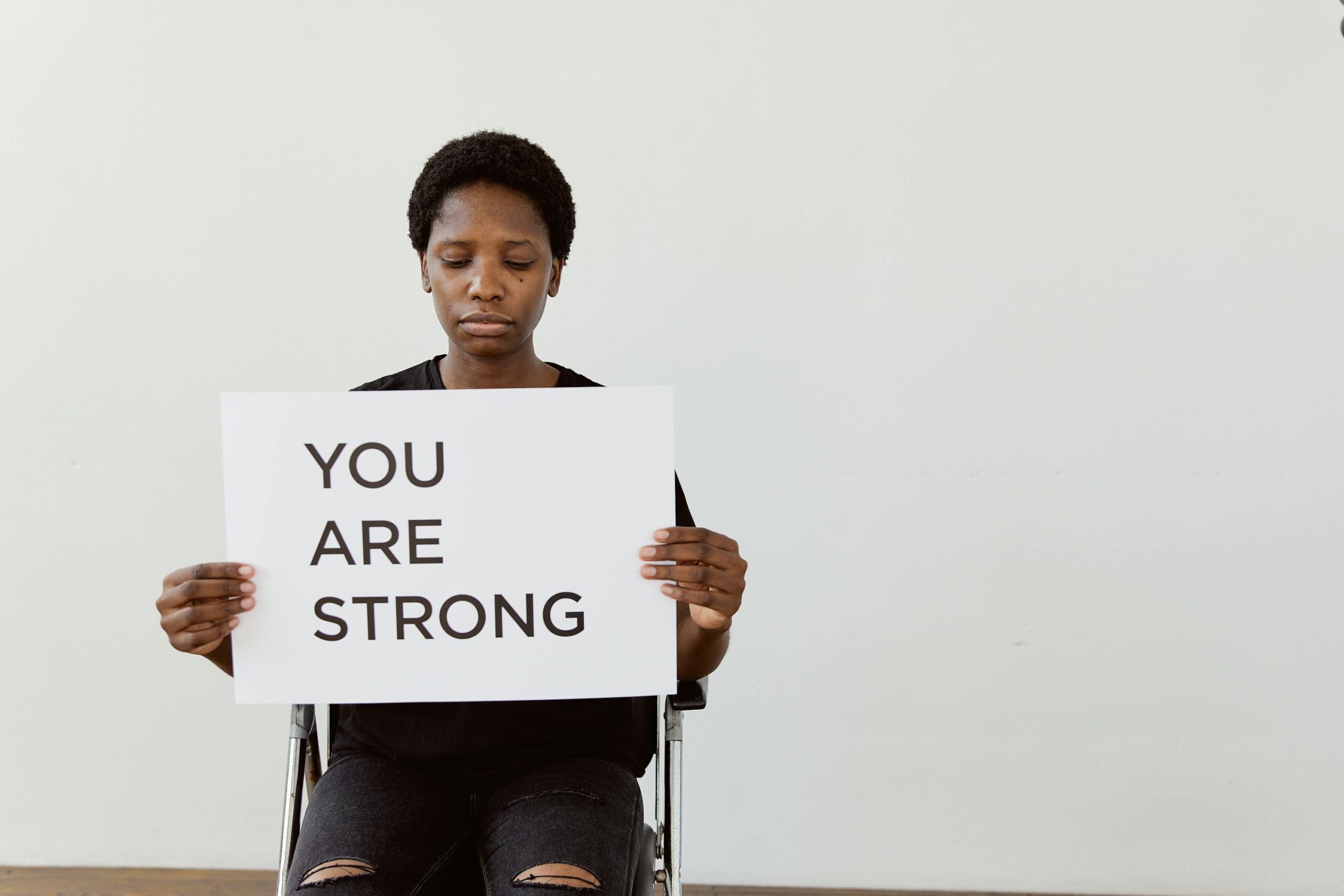A woman holding a card that says "You are strong".