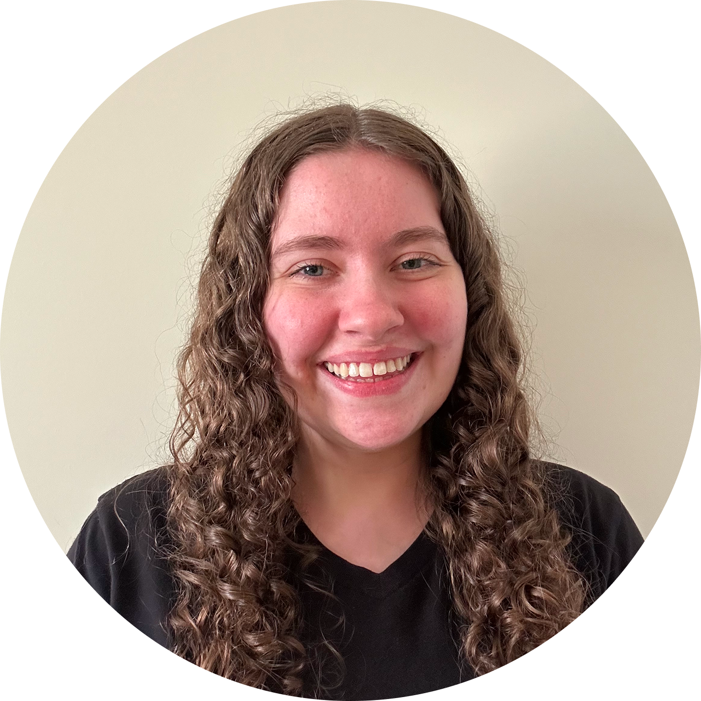 Smiling woman with long curly brown hair in a black shirt, neutral beige circular background.