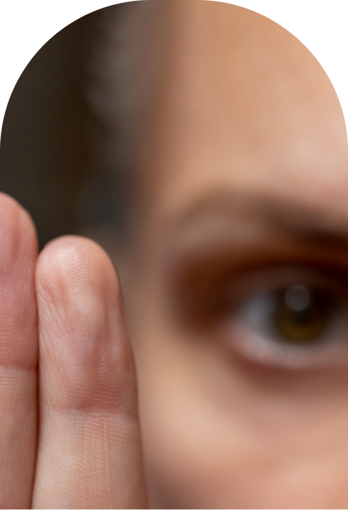 Close-up of a person touching the skin near their eye with two fingers, showing a brown iris in view.