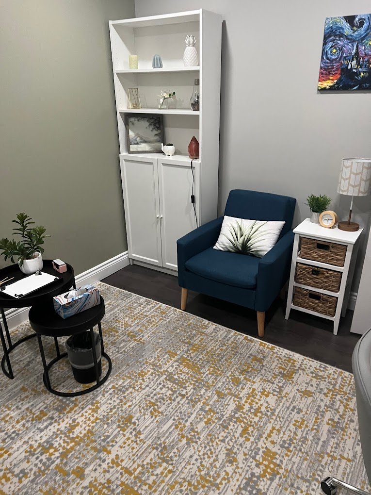 Cozy counselling office with blue armchair and white bookshelf.